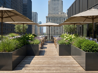 Outdoor seating area with tables, chairs, and umbrellas on a rooftop with city skyline in the background.